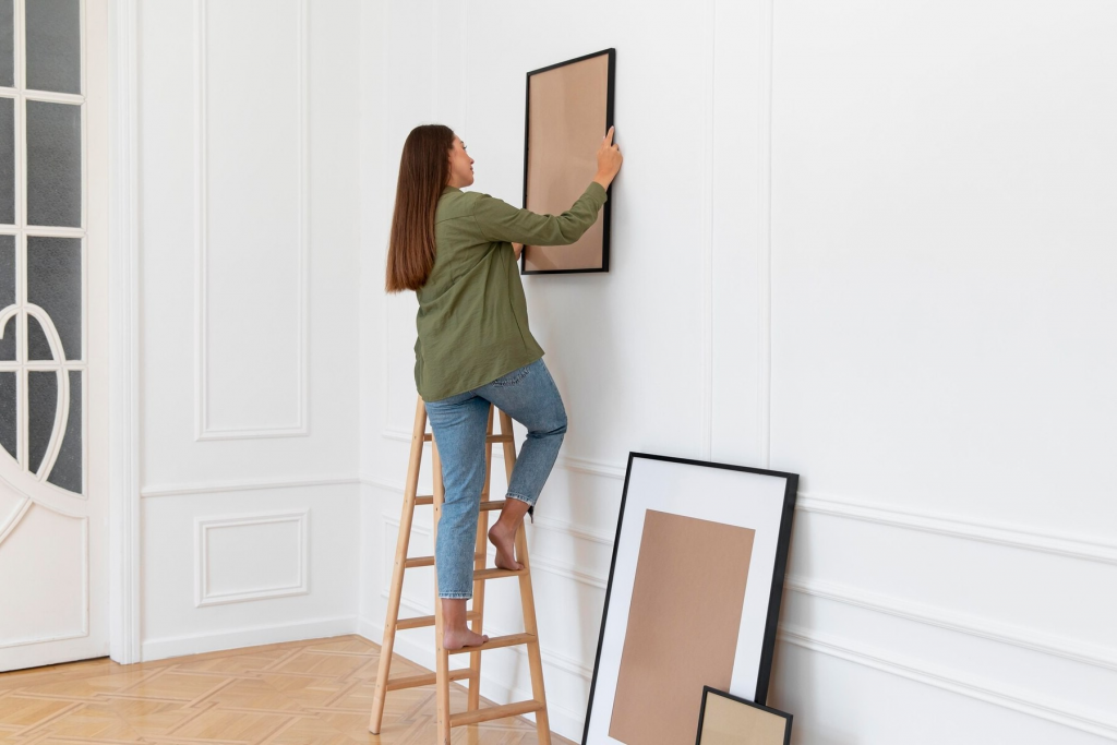 woman hanging pictures on wall of home